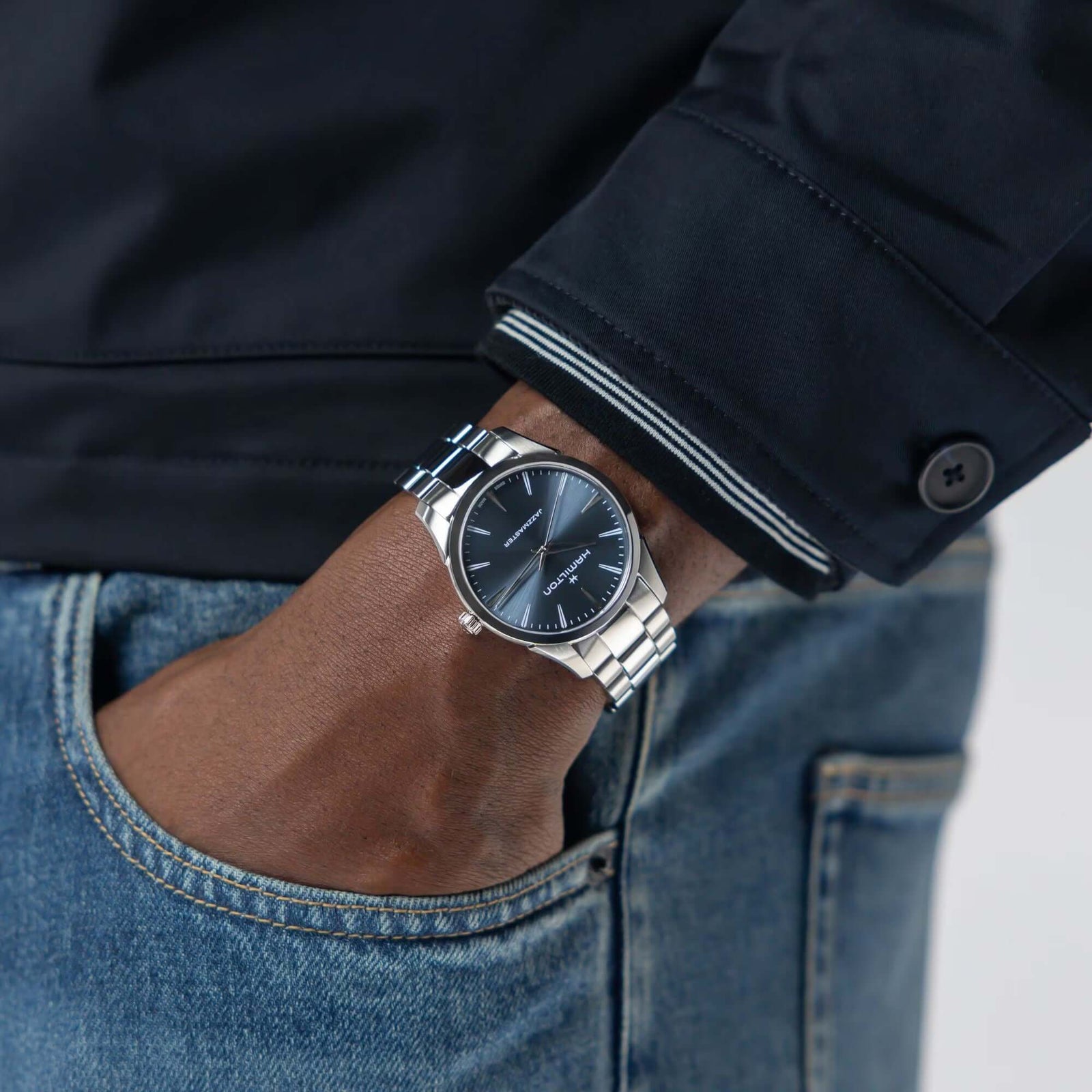 Hand wearing a silver watch with a dark face, against a blurred background.
Hamilton Jazzmaster Quartz 40mm H32461141 Bandiera Jewellers