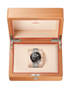 An Omega wristwatch presented inside an open wooden watch box with a cream interior and red trim. The watch has a black dial, silver-toned case, and silver link bracelet.